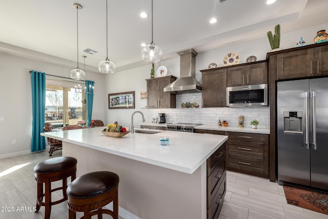 kitchen with wall chimney exhaust hood, visible vents, a breakfast bar, a sink, and stainless steel appliances