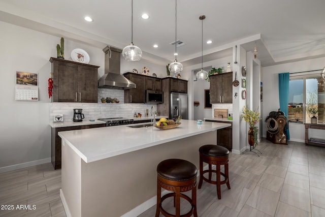 kitchen featuring wall chimney range hood, dark brown cabinets, visible vents, appliances with stainless steel finishes, and a sink