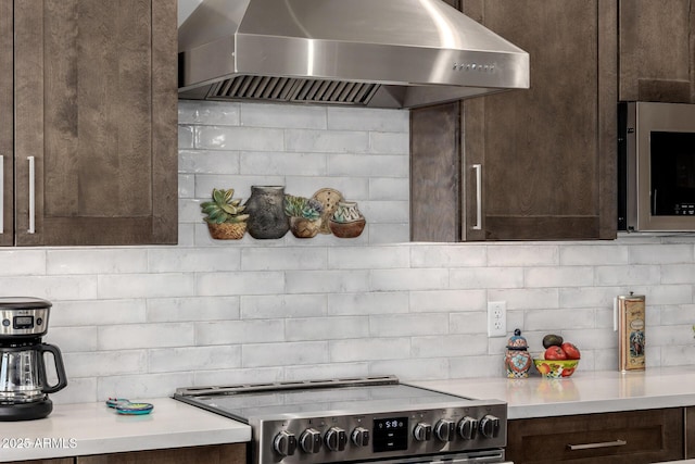 kitchen featuring tasteful backsplash, wall chimney range hood, dark brown cabinets, light countertops, and stainless steel appliances
