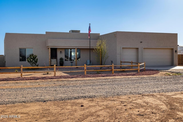 pueblo-style home featuring an attached garage, concrete driveway, stucco siding, and a fenced front yard