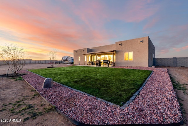 back of property at dusk with a patio area, a fenced backyard, a lawn, and stucco siding
