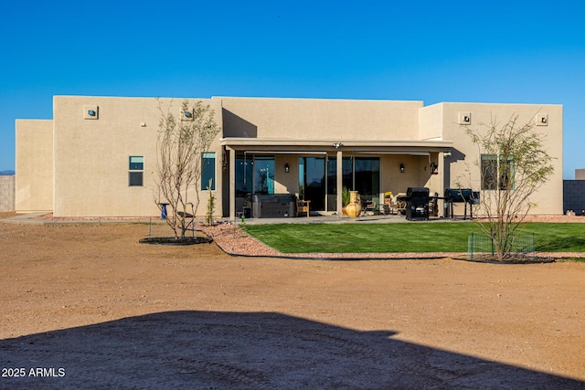 rear view of house with a patio area, stucco siding, a hot tub, and a lawn
