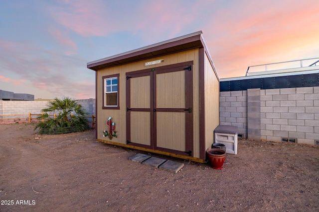 outdoor structure at dusk featuring an outbuilding, a fenced backyard, and a shed