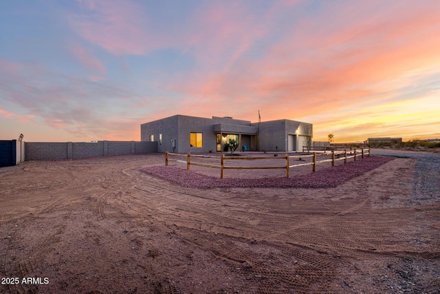 back of house at dusk featuring stucco siding and fence
