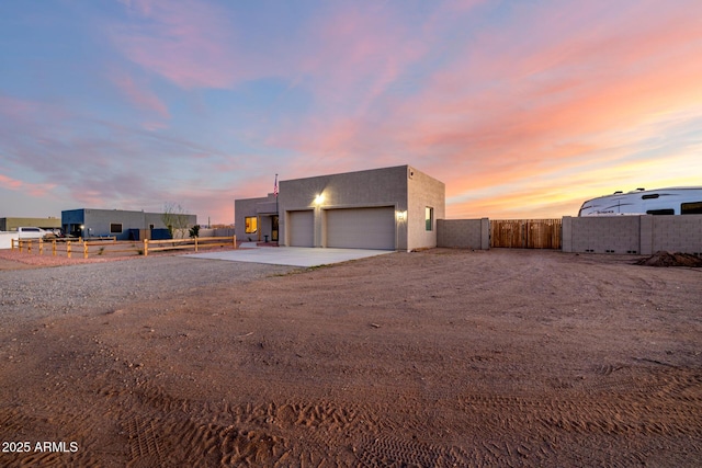 contemporary house featuring dirt driveway, fence, a garage, and stucco siding