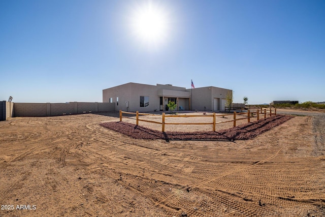 southwest-style home with a rural view, fence, and stucco siding