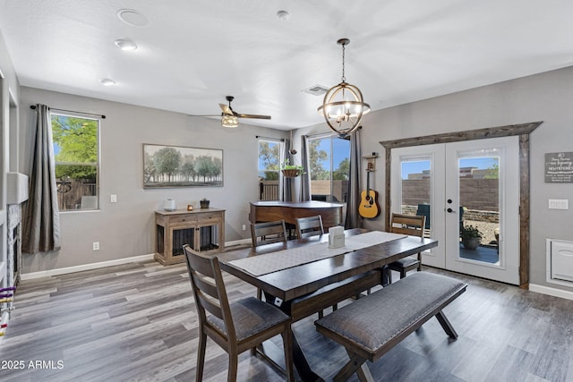 dining space featuring light wood-style flooring, ceiling fan with notable chandelier, baseboards, visible vents, and french doors