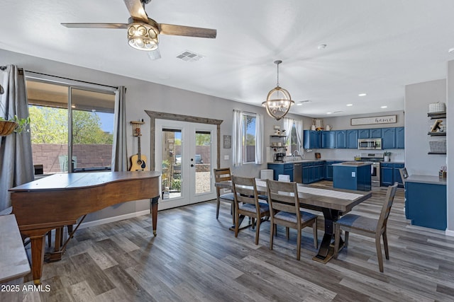 dining space with visible vents, wood finished floors, french doors, and ceiling fan with notable chandelier