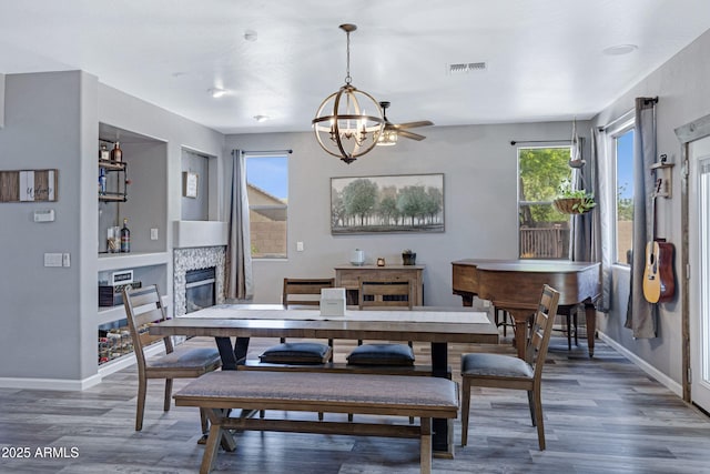 dining room featuring visible vents, baseboards, a glass covered fireplace, wood finished floors, and a notable chandelier