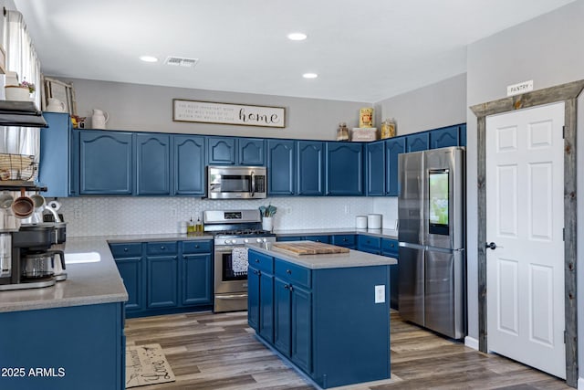 kitchen featuring appliances with stainless steel finishes, wood finished floors, blue cabinetry, and decorative backsplash
