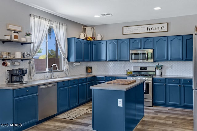 kitchen with blue cabinets, stainless steel appliances, light wood-type flooring, a sink, and visible vents