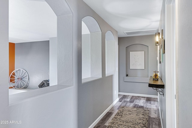 hall featuring arched walkways, wood finished floors, and baseboards