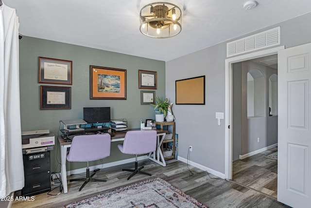 office featuring wood finished floors, visible vents, arched walkways, and baseboards