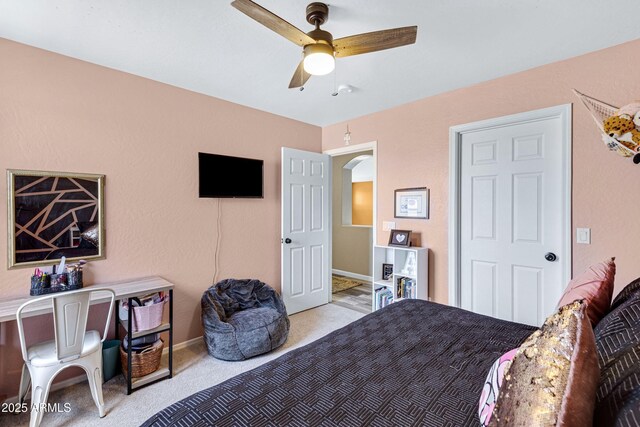 bedroom with arched walkways, ceiling fan, light carpet, and baseboards