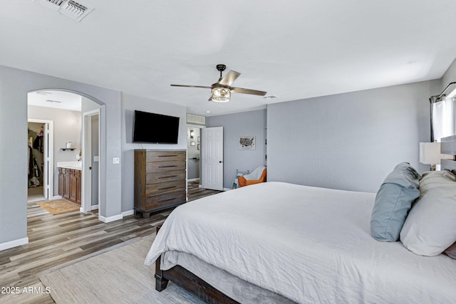 bedroom with wood finished floors, visible vents, baseboards, and arched walkways