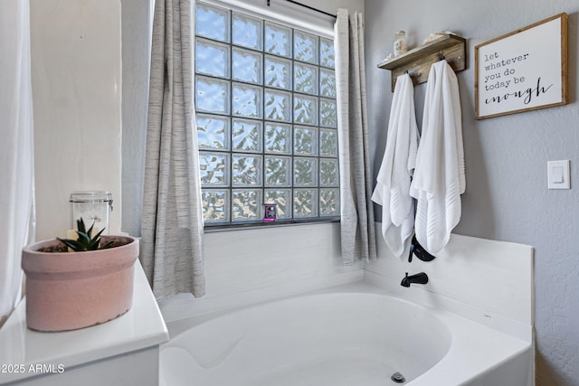 bathroom with a healthy amount of sunlight, a textured wall, and a garden tub