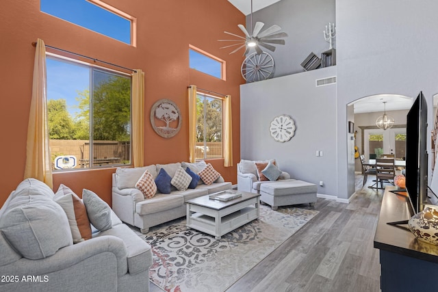 living room with arched walkways, wood finished floors, ceiling fan, visible vents, and a high ceiling