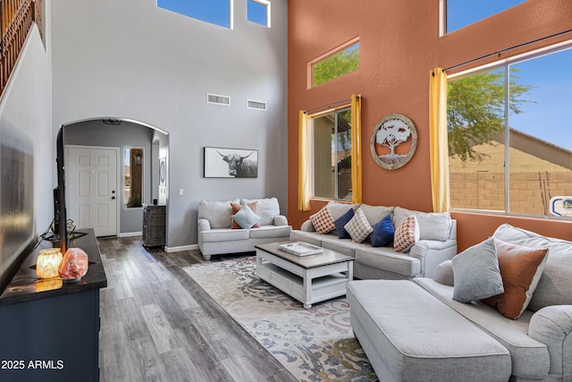 living area featuring wood finished floors, visible vents, a high ceiling, and arched walkways