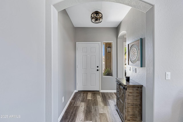 doorway featuring arched walkways, a textured wall, baseboards, and dark wood finished floors