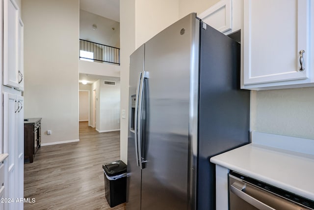 kitchen featuring appliances with stainless steel finishes, light wood-type flooring, white cabinetry, and a high ceiling