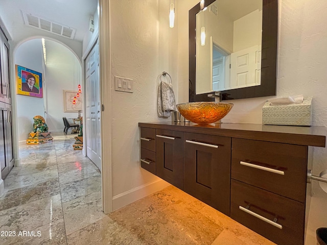 10068 E Turquoise Ave, Scottsdale, AZ 85258 - bathroom with visible vents, stone finish floor, baseboards, vanity, and a textured wall