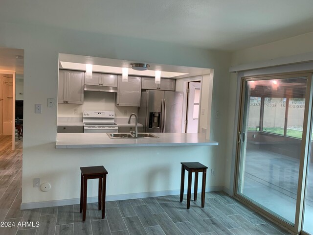 kitchen featuring dark hardwood / wood-style floors, stainless steel fridge with ice dispenser, sink, kitchen peninsula, and stove