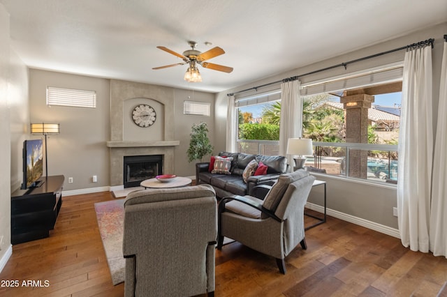 living area featuring a large fireplace, a ceiling fan, hardwood / wood-style flooring, and baseboards