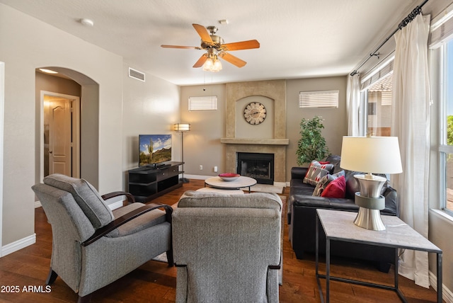 living room with dark wood-style flooring, visible vents, baseboards, a ceiling fan, and arched walkways