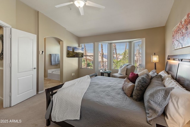 bedroom with connected bathroom, vaulted ceiling, a ceiling fan, light carpet, and arched walkways