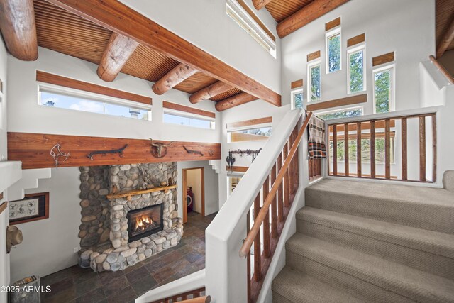 stairway featuring a stone fireplace, wood ceiling, a towering ceiling, stone finish flooring, and beam ceiling