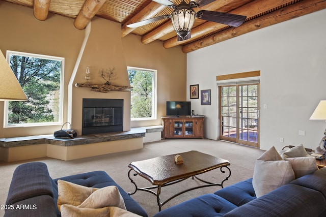 carpeted living room featuring wood ceiling, a ceiling fan, a large fireplace, and beam ceiling
