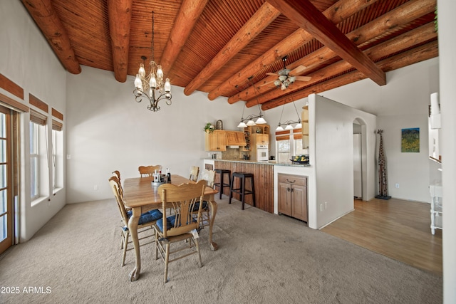 dining space featuring light carpet, beam ceiling, arched walkways, ceiling fan with notable chandelier, and wood ceiling
