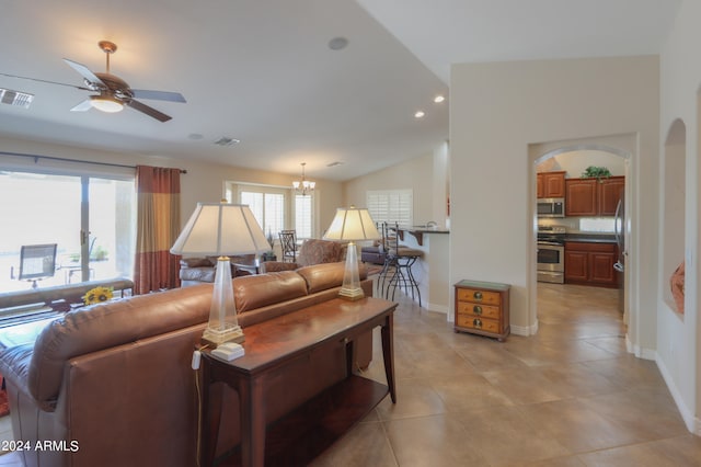 tiled living room featuring ceiling fan with notable chandelier, plenty of natural light, and vaulted ceiling