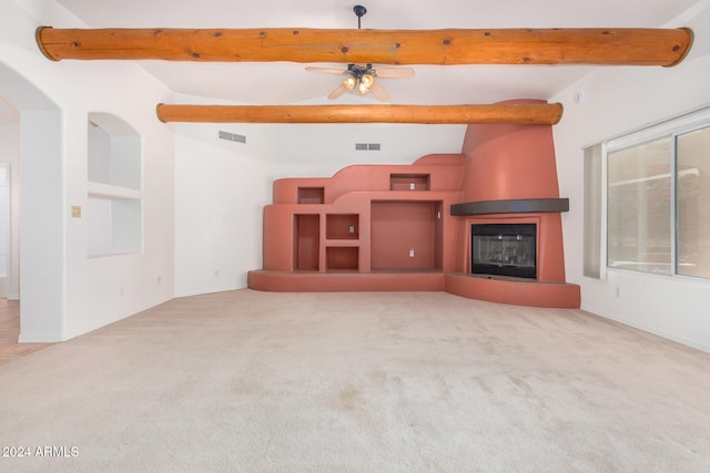 unfurnished living room with ceiling fan, a fireplace, beamed ceiling, and light carpet