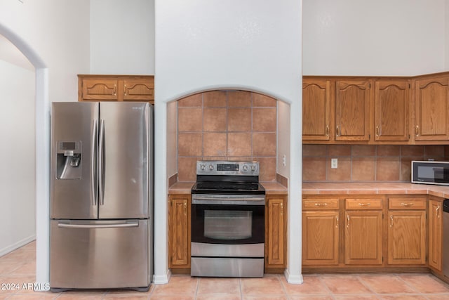 kitchen featuring tasteful backsplash, tile countertops, light tile patterned floors, and appliances with stainless steel finishes