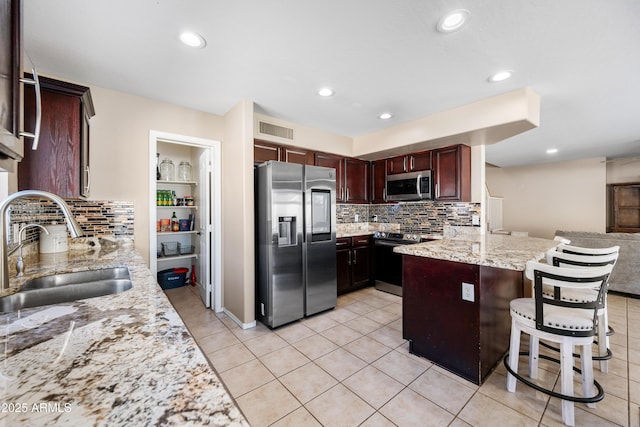 kitchen with light stone counters, a breakfast bar area, stainless steel appliances, visible vents, and a sink