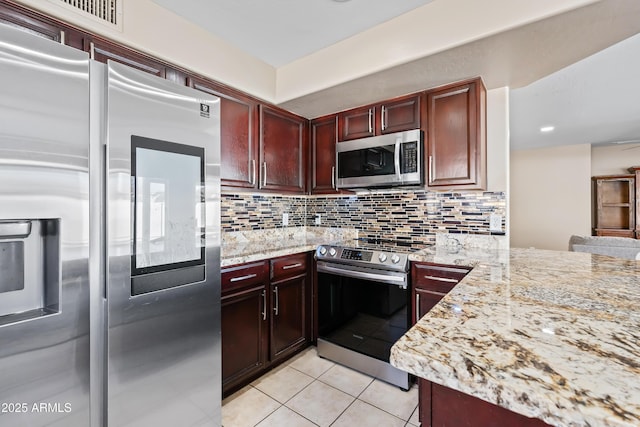 kitchen with light tile patterned floors, tasteful backsplash, appliances with stainless steel finishes, light stone countertops, and dark brown cabinets