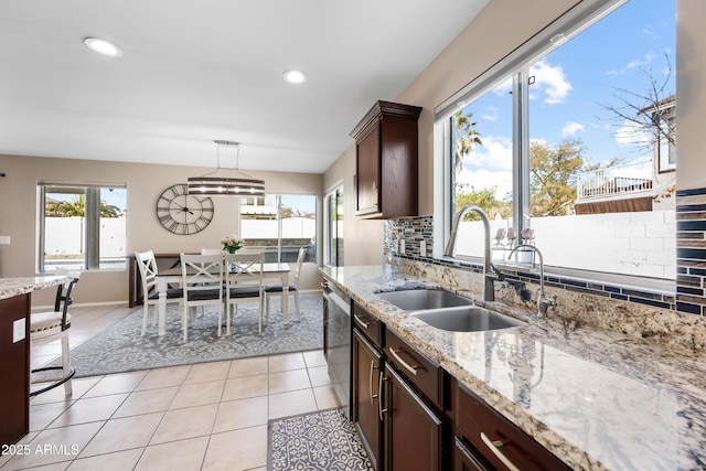 kitchen featuring pendant lighting, light tile patterned floors, tasteful backsplash, stainless steel dishwasher, and a sink