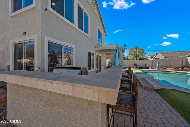 view of patio featuring a fenced in pool, a fenced backyard, exterior kitchen, and outdoor dry bar