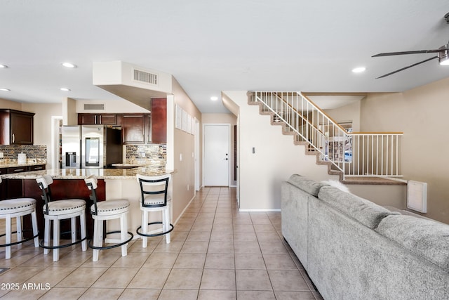 kitchen featuring light tile patterned flooring, visible vents, open floor plan, decorative backsplash, and stainless steel fridge