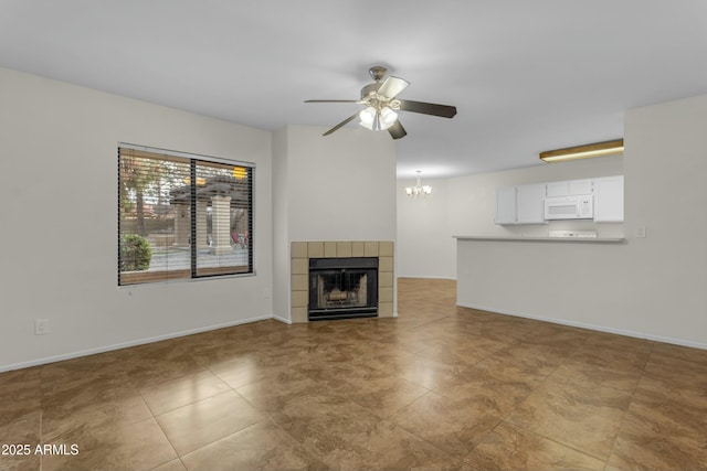 unfurnished living room with a tiled fireplace and ceiling fan with notable chandelier