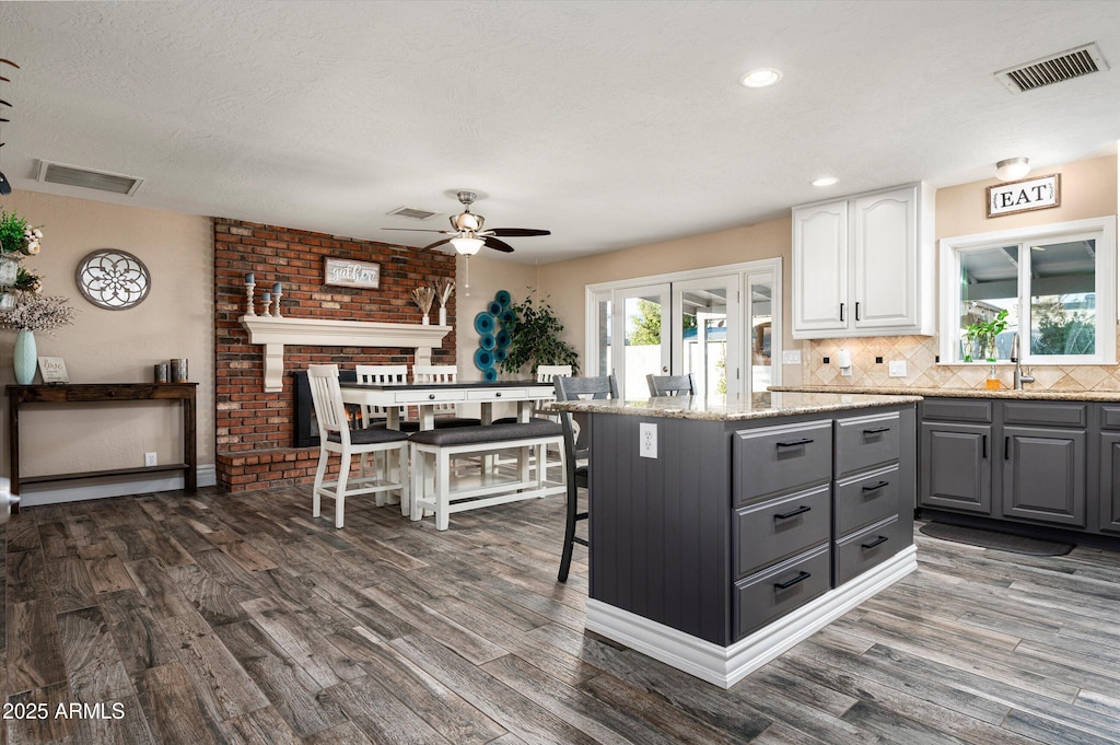 kitchen with gray cabinetry, white cabinetry, light stone countertops, a kitchen island, and dark hardwood / wood-style flooring