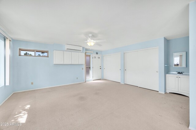 unfurnished bedroom featuring two closets, light colored carpet, a ceiling fan, a sink, and a wall mounted air conditioner