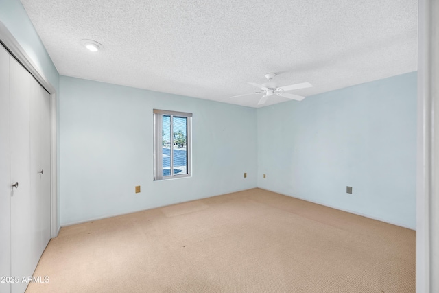 unfurnished bedroom with light carpet, ceiling fan, a closet, and a textured ceiling