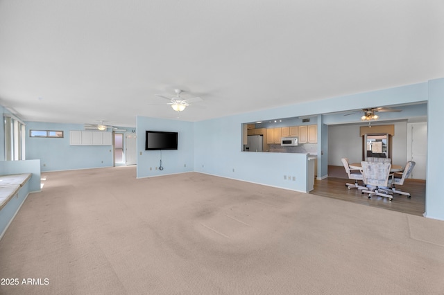 unfurnished living room with a healthy amount of sunlight, a ceiling fan, and light colored carpet