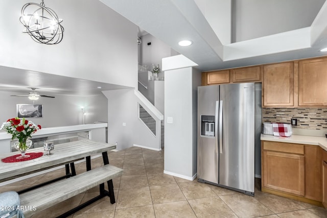 kitchen featuring backsplash, stainless steel fridge, pendant lighting, light tile patterned flooring, and ceiling fan with notable chandelier