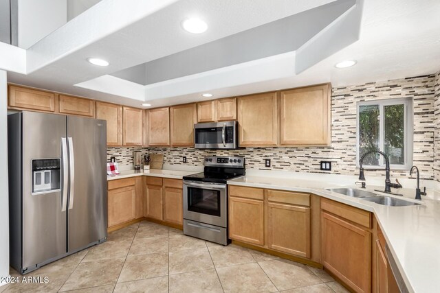 kitchen featuring sink, tasteful backsplash, a tray ceiling, light tile patterned flooring, and appliances with stainless steel finishes