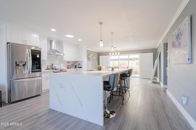 kitchen featuring wall chimney exhaust hood, stainless steel fridge, a kitchen island with sink, and white cabinets