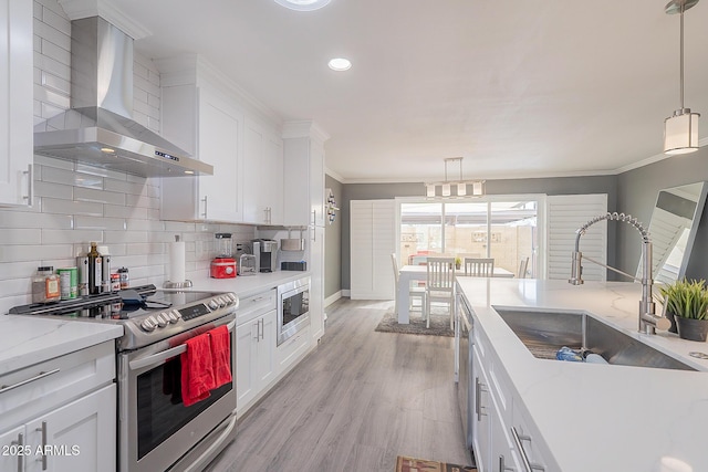 kitchen featuring wall chimney exhaust hood, sink, decorative light fixtures, stainless steel appliances, and white cabinets