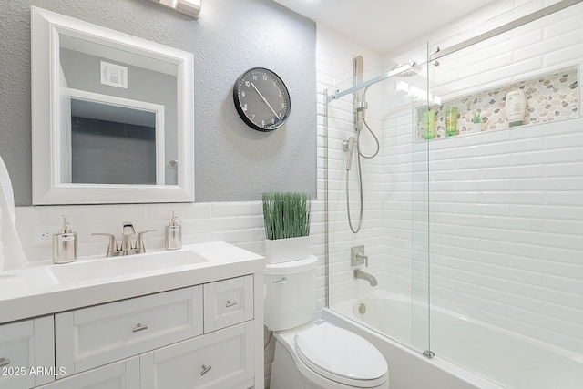 full bathroom featuring vanity, bath / shower combo with glass door, tile walls, and toilet